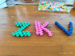 Zeltlager Kolping Velbert 2025 - Auf dem Tisch liegen kleine Entchen-Figuren. Sie sind farblich Sortiert in türkis, lila und dunkelblau und aneinander gereiht. Sie bilden die Buchstaben Z, K und V für Zeltlager Kolping Velbert