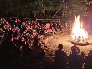 Zeltlager Kolping Velbert - Die Kinder des Kolping-Zeltlagers sitzen abends im Halbkreis um ein hell lodenrdes Lagerfeuer im Freien. Es ist das Abschlussfeuer.